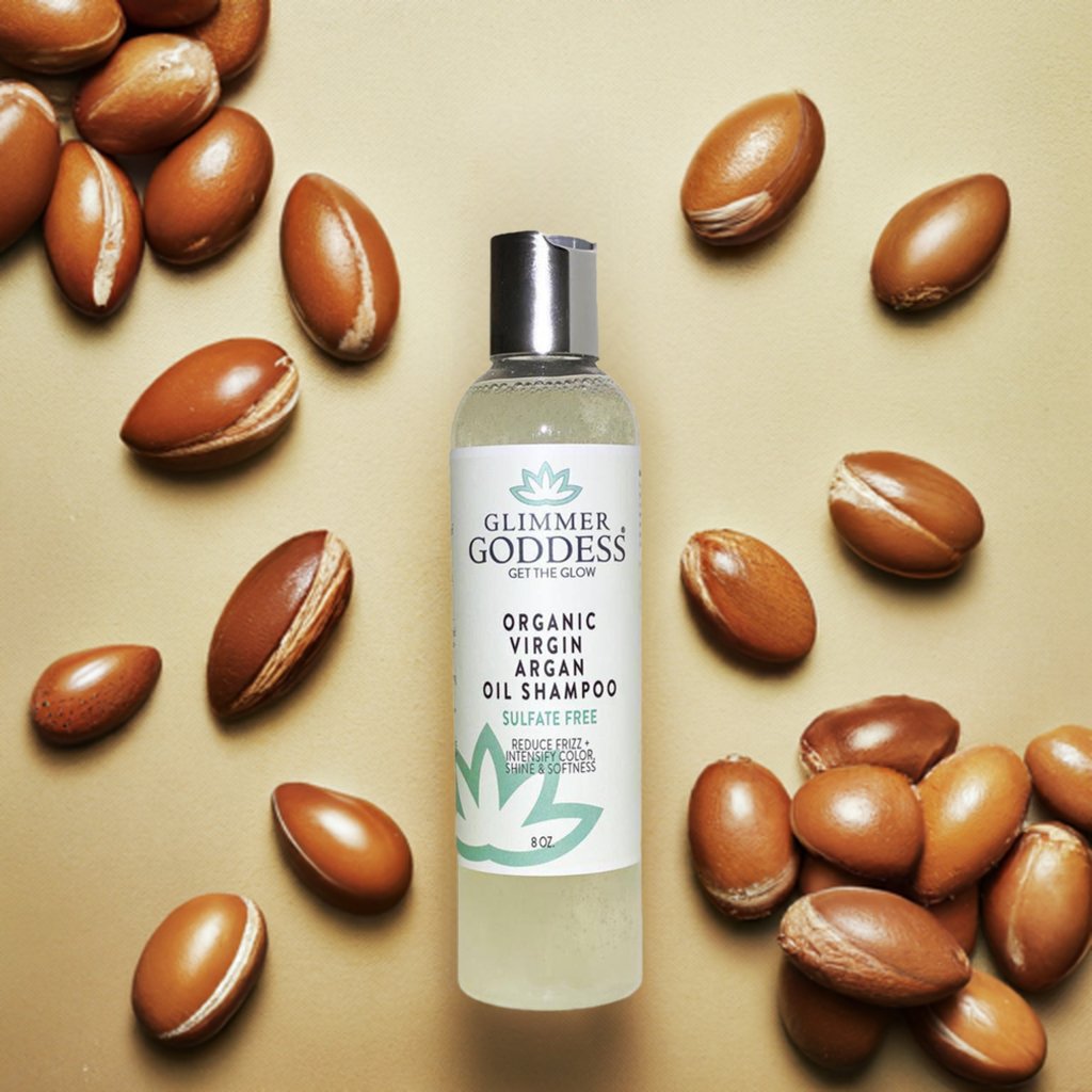 Glimmer Goddess shampoo bottle surrounded by argan oil seeds on a beige background